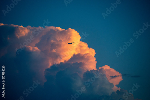 Silhouetted airplane navigating past a colossal cumulus cloud illuminated by sunset light. For overcoming business obstacles, navigating uncertainty, corporate resilience, ambitious goals