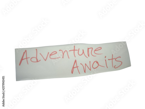 Foto Handwritten note with the words adventure awaits written in red ink on paper iso
