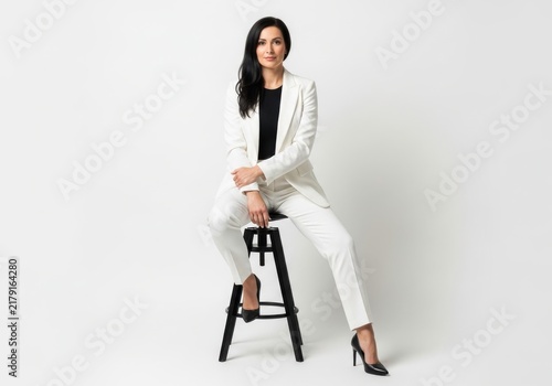 Woman in white suit sitting on stool with magazine