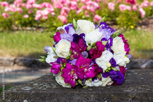 Colorful wedding bouquet resting on stone with roses in background