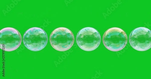 Row of iridescent soap bubbles floating horizontally on green screen background
