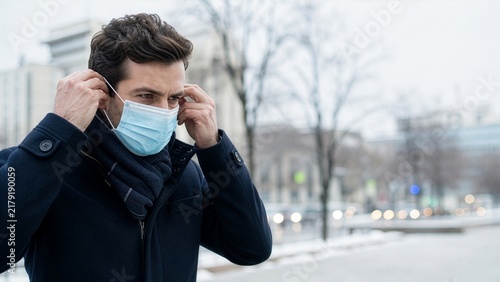 Man putting on a protective face mask outdoors in winter city during cold and flu season, illness prevention and public health protection concept