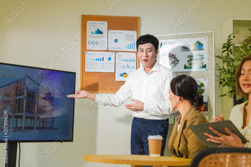 Obraz na płótnie The presenter turns back to his colleagues while pointing at the display, inside a bright eco friendly architecture studio in Thailand, young Asian professionals planning a green building