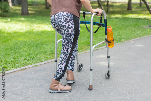 A young woman with cerebral palsy walks in a park with a walker.