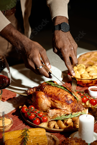 Vertical image of African American man carving roasted turkey during Thanksgiving dinner with friends. Scene represents holiday celebration  suitable for festive food marketing