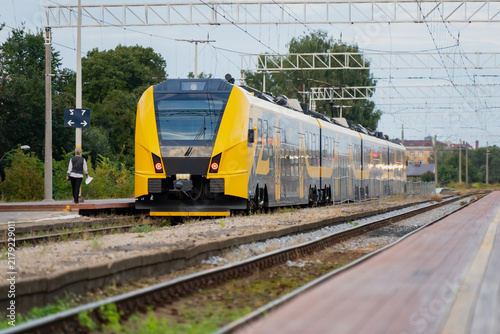 Konstfotografi Commuter rail schedules hinge on moments like this one, a yellow regional train rolling toward the platform as a lone passenger waits near the signal post