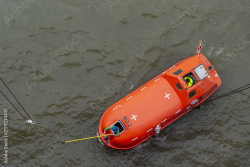 Fotografie Small rescue boat maneuvering close to a large ship during an emergency drill, with the crew preparing to secure the boat to the vessel's lifting hooks