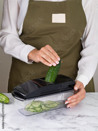 Фотография Woman slicing fresh cucumber into thin slices using manual mandoline slicer with