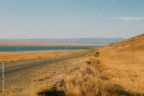 Fotografie Long empty asphalt road running alongside river Irtysh shore through dry steppe hills in East Kazakhstan
