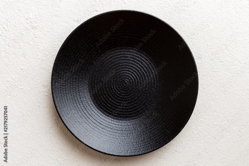 Obraz premium Top view of black plate on cement background. Empty space for your design