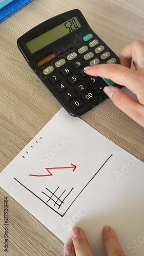 a paper with a falling red arrow chart and calculator calculations in the background, decreasing revenue, financial losses, low income and economic downturn.
