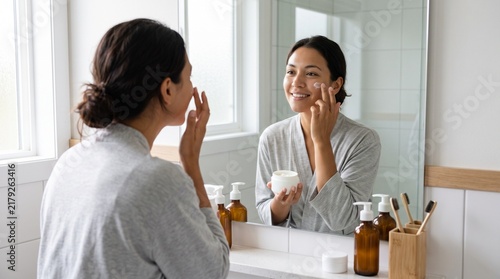 Woman Applying Face Moisturizer in Front of Bathroom Mirror