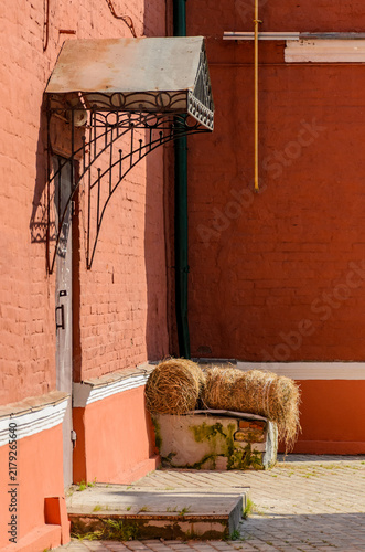 Straw bales under metal canopy near red brick wall on sunny day