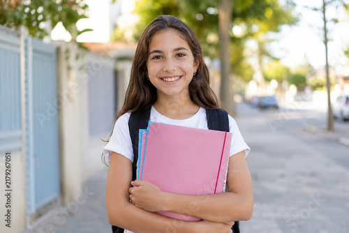 Niña feliz camino del colegio con carpeta y mochila escolar: primer día de clase, vuelta al cole, educación, infancia y regreso a la rutina escolar