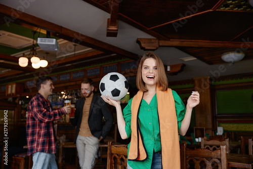 Fotografie Woman exuberantly elevates football above her head amidst jovial gathering with