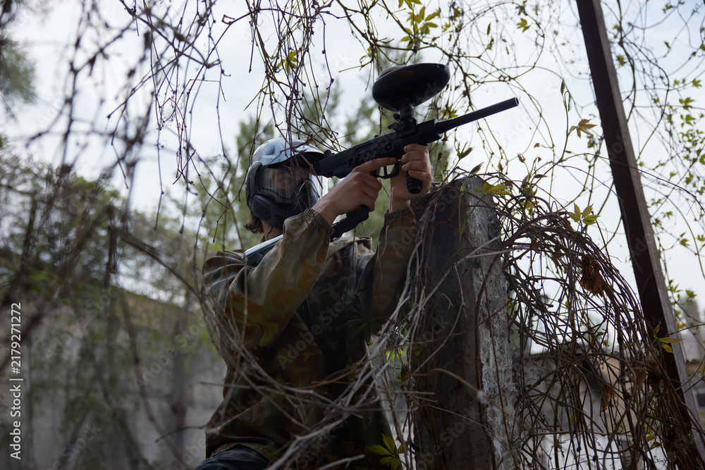 Obraz premium Confident soldier aims a paintball gun while hiding in the dry trees