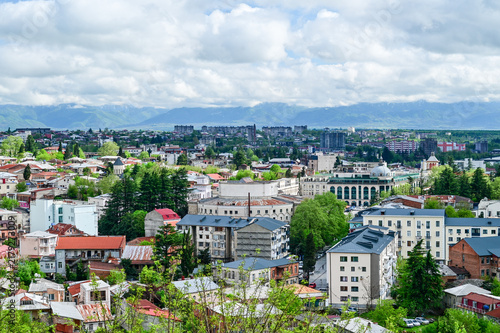 Panoramic view of the Old Town of Kutaisi with its traditional houses, church towers, and green hills under a partly cloudy sky, Imereti region, Georgia