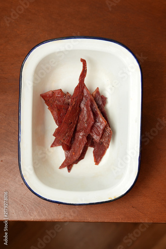 Canvastavla Beef jerky strips in enamel dish on wooden table close up