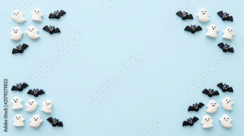 Halloween background with small white ghost and black bat figurines arranged in corners on light blue