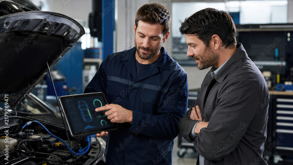 Fototapeta premium Mechanic showing car computer diagnostic results on tablet to client in auto repair shop. Vehicle engine inspection with digital technology. Professional automotive service and maintenance concept.