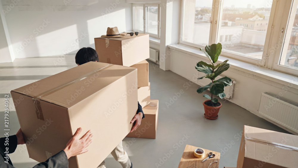 Fototapeta premium People carrying large cardboard boxes moving into new house or apartment interior design project.