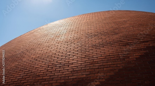 Abstract curved red brick wall texture, modern architectural design detail, low angle view of masonry surface under blue sky, construction material pattern for urban building
