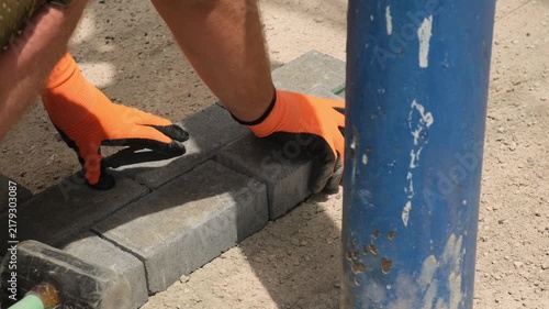 Road construction worker lays paving stones along a taut guide string and adjusts them with a rubber mallet. Paving installation, municipal work, alternative to asphalt, public infrastructure.