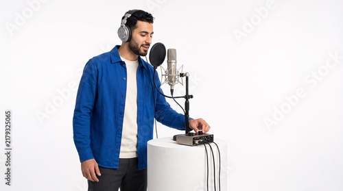 Man in blue shirt recording audio with professional microphone and headphones in studio
