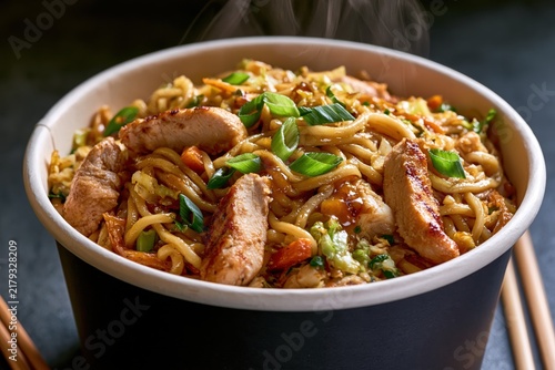 Steaming Asian stir-fried noodles with grilled chicken strips in bowl