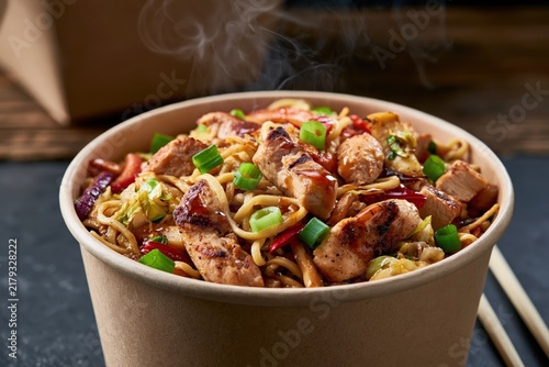Steaming grilled chicken pieces on vegetable stir-fried noodles in bowl