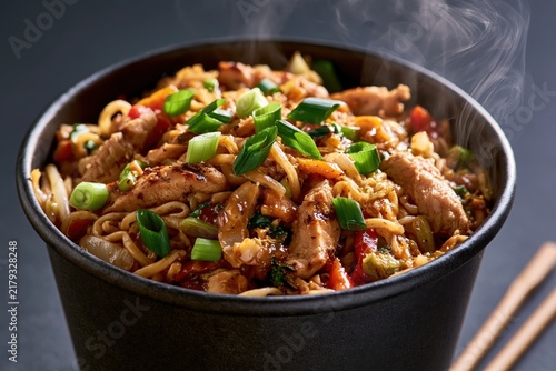 Steaming bowl of stir-fried noodles with grilled chicken and vegetables