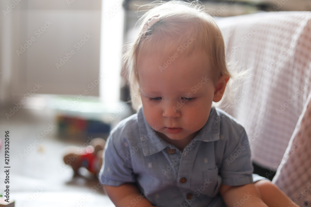 Fototapeta premium Young child with blonde hair looking down thoughtfully indoors