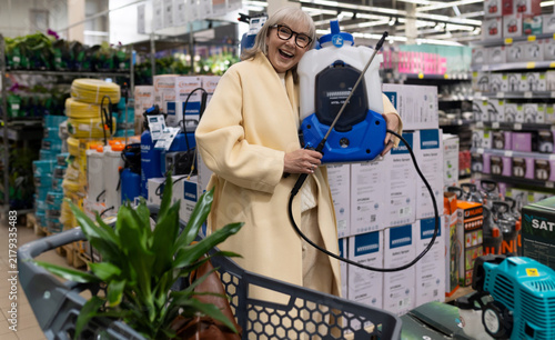 Cheerful senior woman holding a garden sprayer while shopping for gardening equipment in a store