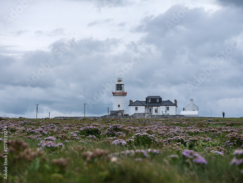 Photography Lighthouse stands tall on grassy hill under cloudy sky