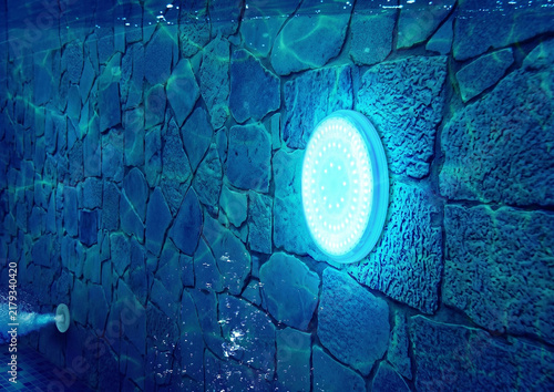 Close up underwater view of a large bright LED light mounted on a rustic stone wall pool