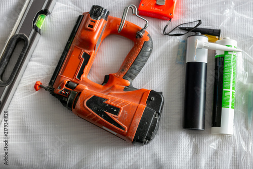 Konstfotografi Collection of trade tools and construction supplies arranged on a textured white protective sheet, including a cordless brad nailer, spirit level, sealants, and tape measure