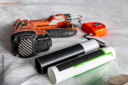 Canvastavla Collection of trade tools and construction supplies arranged on a textured white protective sheet, including a cordless brad nailer, spirit level, sealants, and tape measure