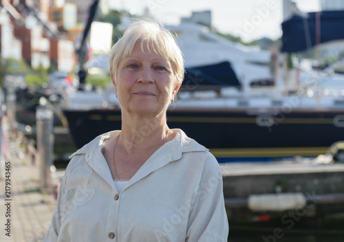 Portrait of a mature woman standing near marina in sunlight.