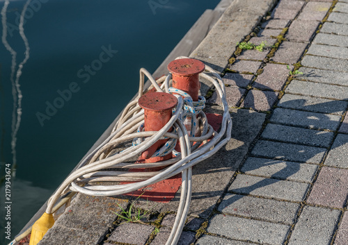 Harbor mooring bollards with coiled rope beside waterfront dock