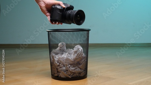 Bild auf Leinwand Hand discarding a black digital slr camera with a lens into a metal mesh trash b