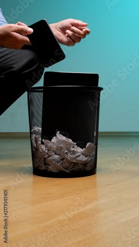 Photography Person's hand dropping a modern smartphone into a mesh trash can filled with cru