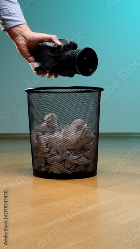 Foto Hand dropping a dslr camera into a metal mesh waste bin filled with crumpled pap