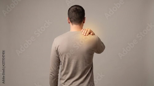 Man touching his painful upper back and shoulder, suffering from muscle tension or injury.