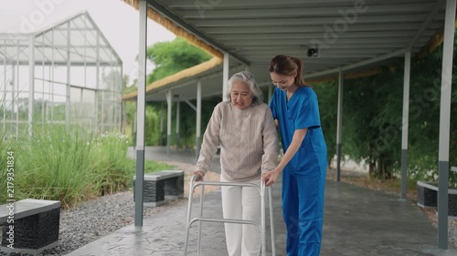 Young caregiver supporting elderly woman with walker in summer garden