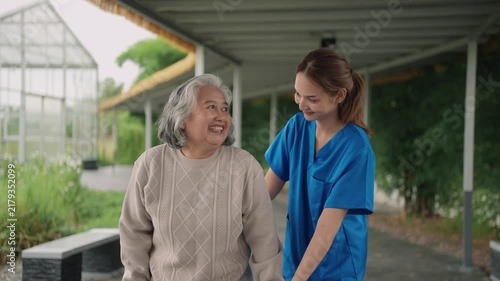 Young caregiver supporting elderly woman with walker in summer garden