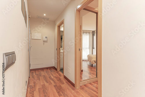 Apartment entrance hallway with wood flooring, an intercom system, and open doors leading to a bedroom and bathroom.