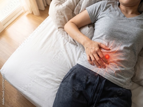 Woman experiencing stomach pain lying in bed with hand on abdomen.