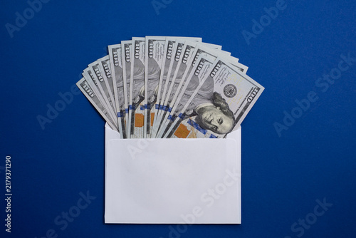 Картината върху платно Fan of 100 US Dollar banknotes inside a white envelope on a blue background, con