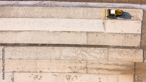 Aerial view of a yellow road roller compacting concrete sections at a construction site in Sleman, Special Region of Yogyakarta, Indonesia.