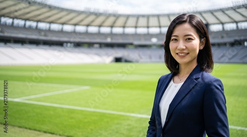 Tapety artystyczne プロフィール写真をイメージした、天然芝のサッカースタジアムのピッチを背にして穏やかな笑顔をカメラに向けている、知的な印象の20代日本人女性社員のバストアップポートレート